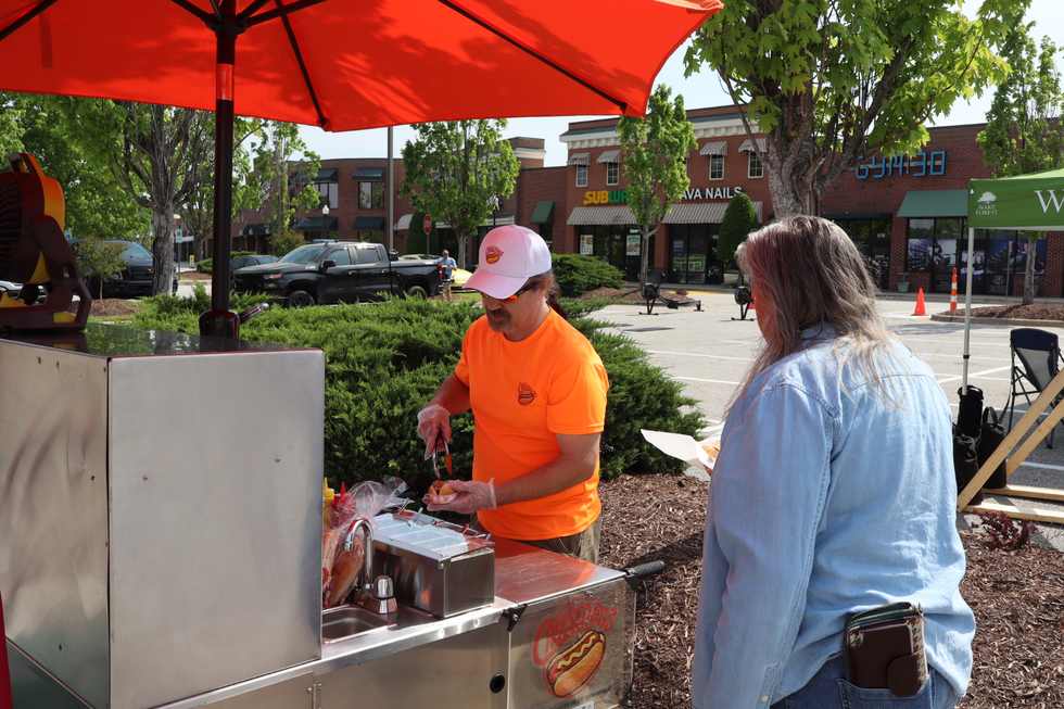Cheesedogs cart serving a line of guests under red umbrellas